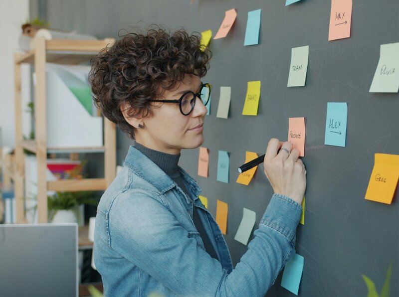 A woman writing a task on a post-it note, on a wall